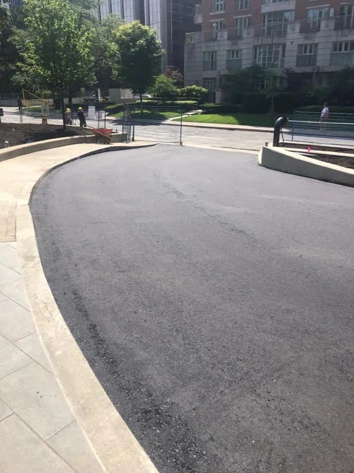 Freshly paved asphalt driveway with new concrete curb at an apartment building